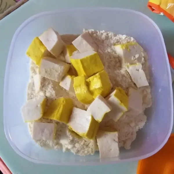 Siapkan tahu, kemudian potong dadu. Dalam wadah masukan tepung serbaguna, kemudian masukan potongan tahu, aduk rata.
