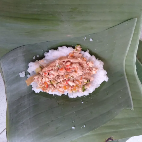 Letakkan nasi secukupnya di atas daun pisang, tambahkan isian di atasnya, letakkan lagi nasi di atas isian. Gulung dan kunci dengan tusukan.