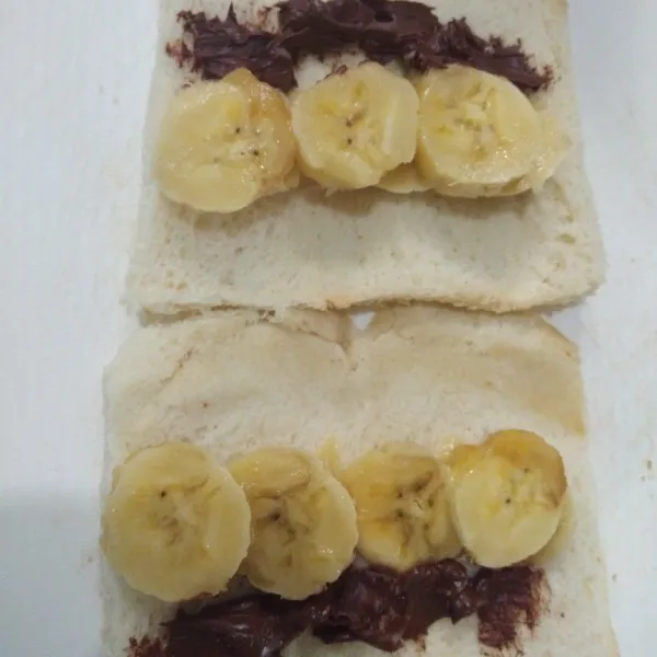 Beri isian coklat dan pisang pada masing-masing roti tawar yang sudah dipipihkan.