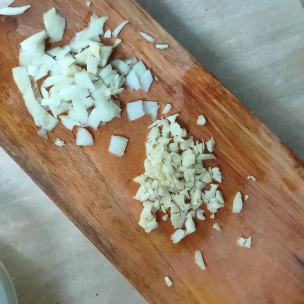 Cincang bawang bombay dan bawang putih.