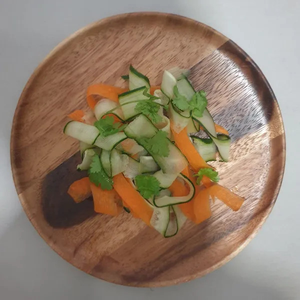Susun mentimun, wortel dan daun ketumbar di atas piring.