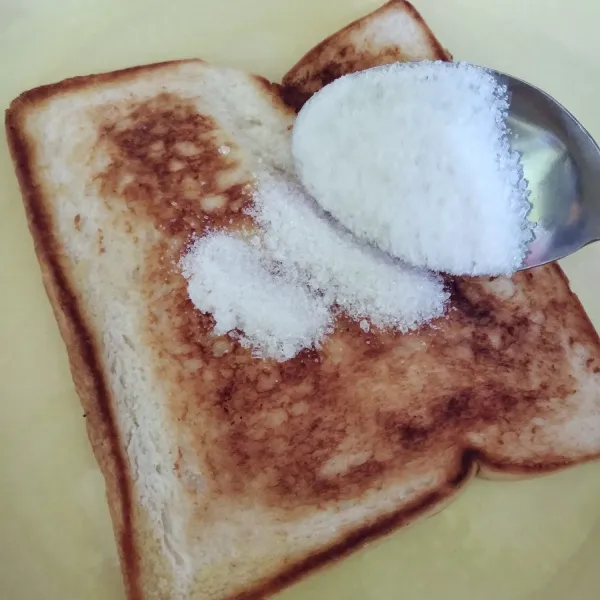 Ambil satu lembar roti tawar panggang, taburi gula pasir.