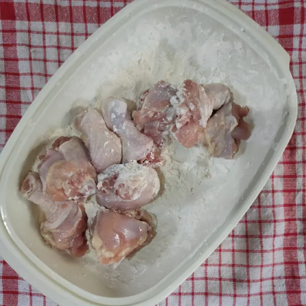Siapkan tepung terigu dalam wadah, lalu balurkan ayam hingga merata.