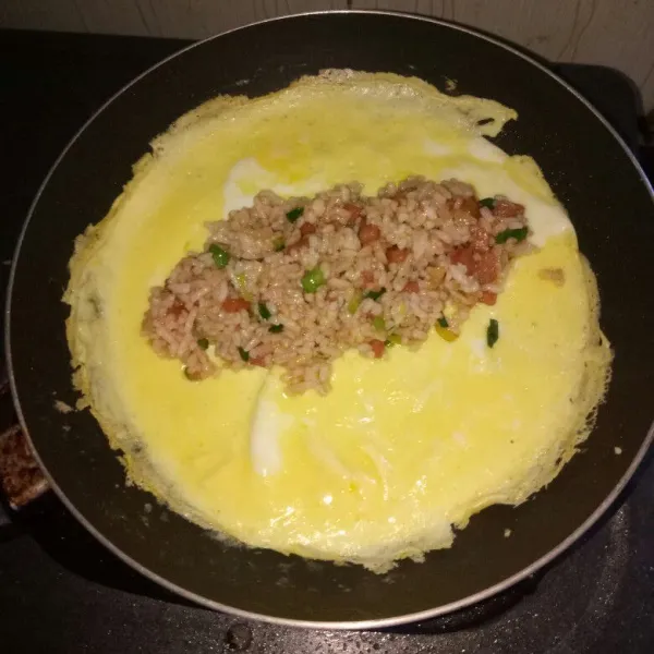 Siapkan pan, lelehkan margarin. Dadar telur dan ratakan keseluruh permukaan pan. Tunggu sampai setengah matang, masukkan nasi goreng tadi lalu lipat sesuai selera. Masak sampai telur matang, angkat dan sajikan dengan topping.