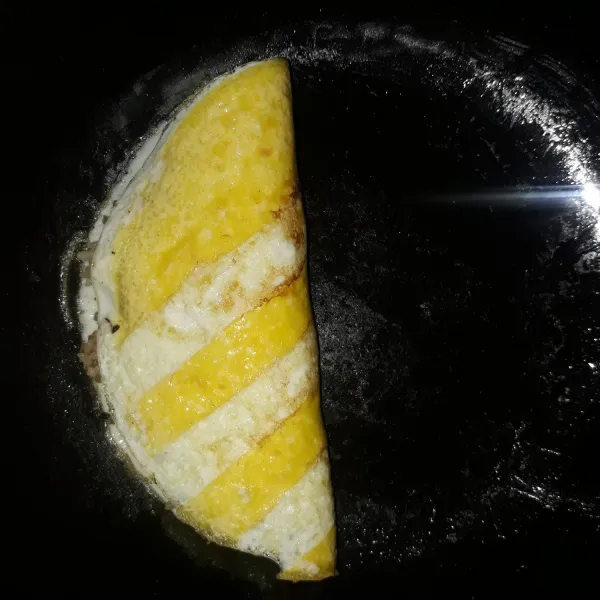 Lipat omelet telur sampai menutupi seluruh nasi goreng. Angkat, lalu sajikan dengan saus sambal dan sayuran.