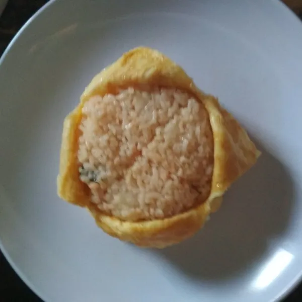 Ambil piring, letakkan di atas mangkuk berisi omurice, lalu balikkan posisinya agar omurice keluar dari mangkuk. Belah permukaan atasnya secara menyilang lalu dibuka agar nasi terlihat. Terakhir, hias dengan taburan daun bawang, bawang goreng dan saus sambal. Omurice siap disajikan.