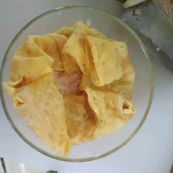 Ambil mangkuk kecil, taruh telur dadar diatasnya, lalu masukkan nasi di atas telur. Padatkan, lalu lipat pinggirannya hingga menutupi nasi goreng.