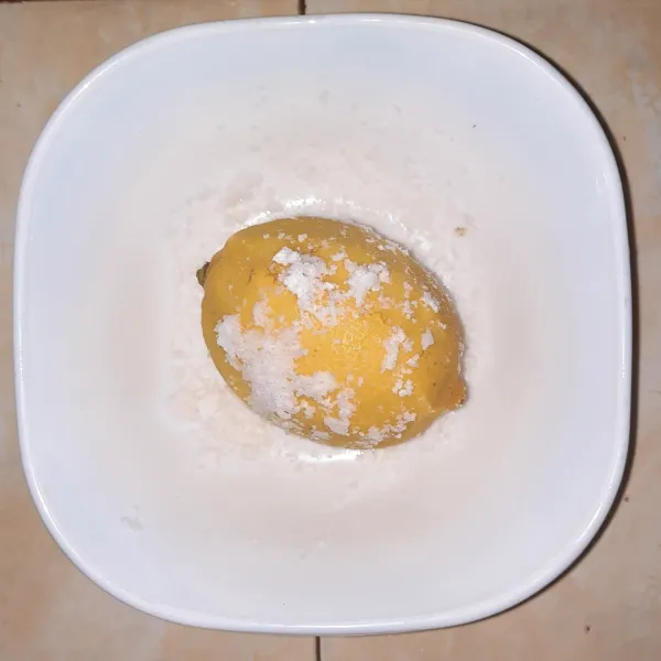 Campur garam dan baking soda. Gosokan pada campuran garam dan baking soda ke permukaan lemon, supaya lapisan lilinnya hilang. Cuci bersih lemon.