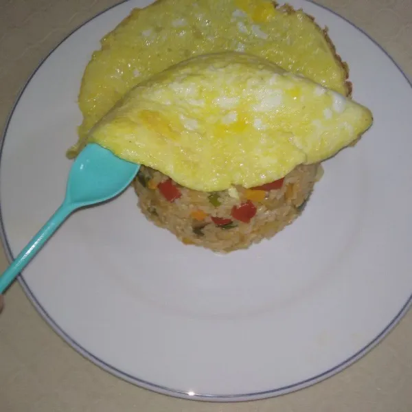 Selimuti nasi dengan omelet ,lipat semua sisi Omelet hingga membungkus semua nasi goreng. Setelah terbungkus omurice siap sajikan.