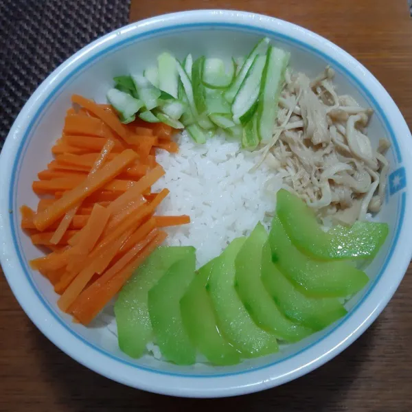 Siapkan nasi hangat dalam mangkuk. Tata wortel, labu siam, jamur dan timun dibagian pinggir mangkok.