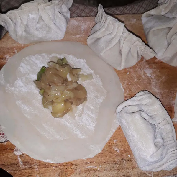 Siapkan kulit pangsit, lalu beri isian secukupnya. Tangkup menjadi setengah lingkaran, lalu lipat dan tumpuk sisinya.