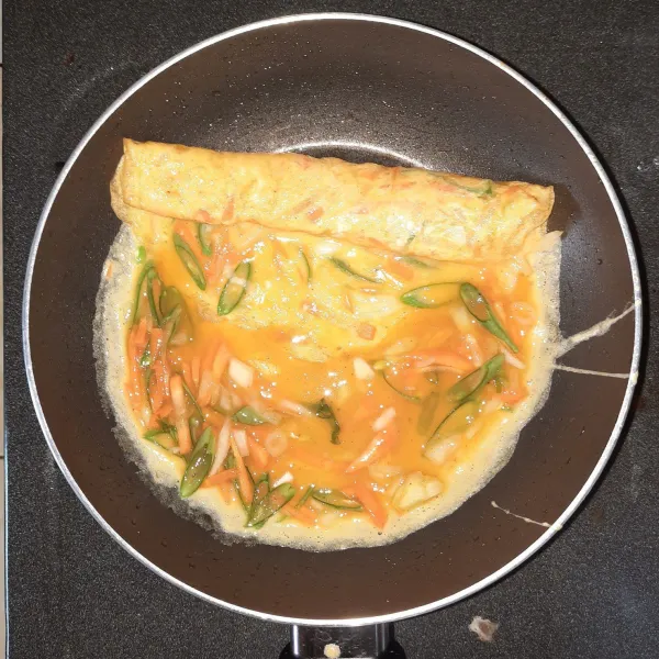 Tambahkan lagi adonan telur sebanyak ½ sendok sayur untuk menutupi bagian kiri, masak sampai setengah matang, lalu digulung seperti langkah sebelumnya.