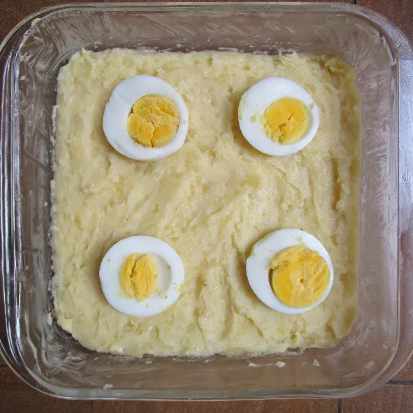 Siapkan loyang/cetakan yang sudah dioles margarin. Tata adonan kentang di dasar loyang. Ratakan. Beri potongan telur rebus di atasnya.