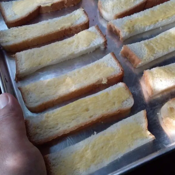 Letakan roti tawar ke ke dalam loyang. Oleskan permukaan roti dengan margarin dan susu