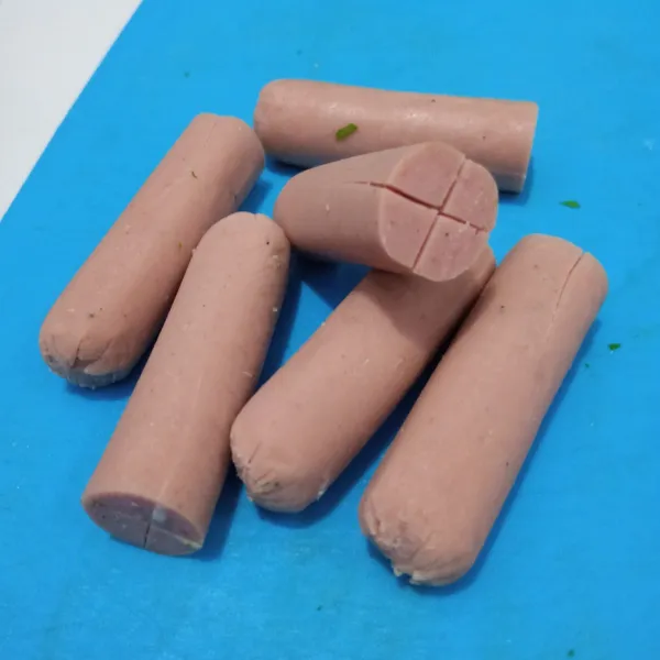 Potong sosis jadi dua. Kemudian kerat bagian bawahnya menjadi empat.