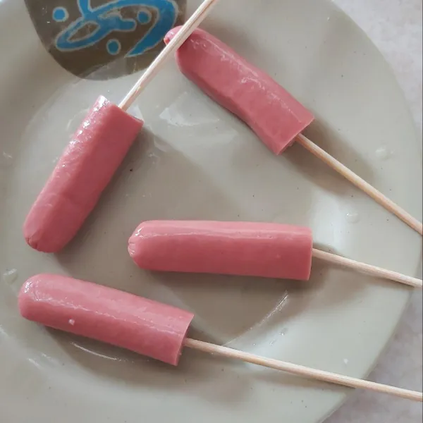 Potong sosis jadi dua lalu tusuk pakai tusuk sate.