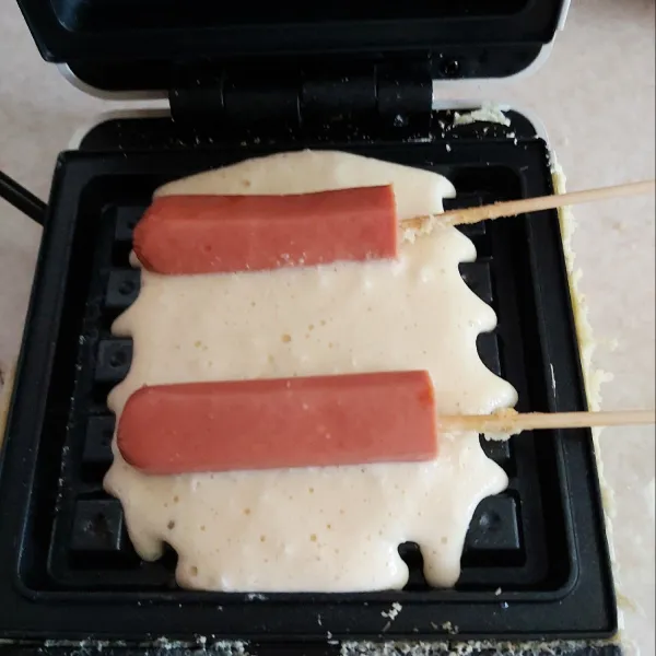 Panaskan cetakan waffle oles tipis dengan butter, tuangi adonan 1/2 cetakan lalu beri sosis.