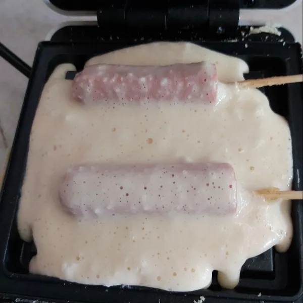 Kemudian tuangi lagi adonan hingga menutupi sosis, kemudian tangkupkan penutup cetakan.