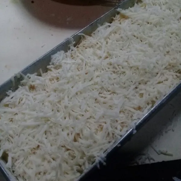 Tuang pada loyang 22x10 yang sudah diolesi margarin dan ditaburi tepung, ratakan beri topping keju parut
