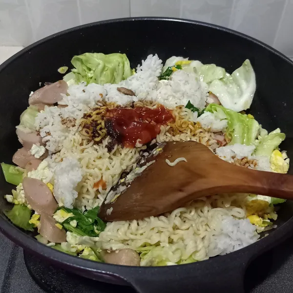 Masukkan nasi putih dan mie, kemudian tambahkan semua bumbu mie, kecap manis dan saos sambal/tomat, aduk sampai rata.