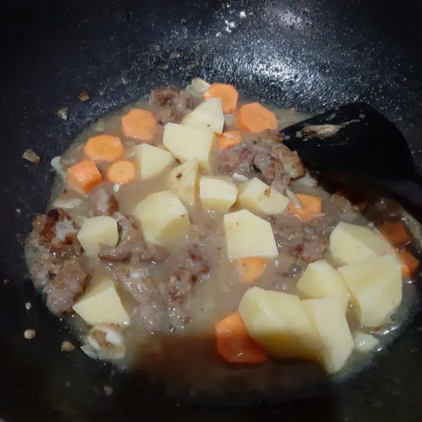 Masukkan potongan kentang dan wortel. Masukkan sisa air ke dalam wajan.