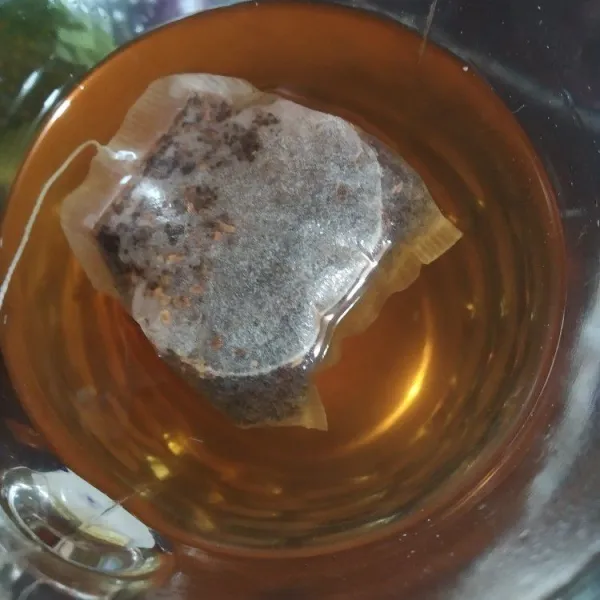 Masukan gula pasir dan teh celup ke dalam gelas lalu seduh dengan air panas, aduk rata sampai gula larut.