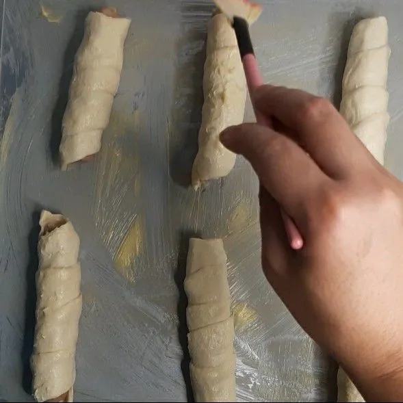 Letakkan sosis roll di baki oven, usahakan untuk memberikan jarak di antara sosis roll agar tidak menempel saat dipanggang. Oleskan salted butter/margarin pada sosis roll.