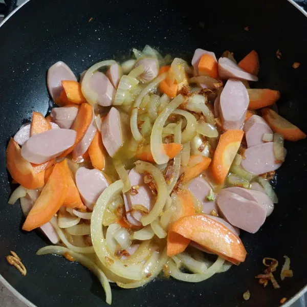 Masukkan wortel dan sosis, tambahkan dengan sedikit rata. Masak hingga setengah matang.