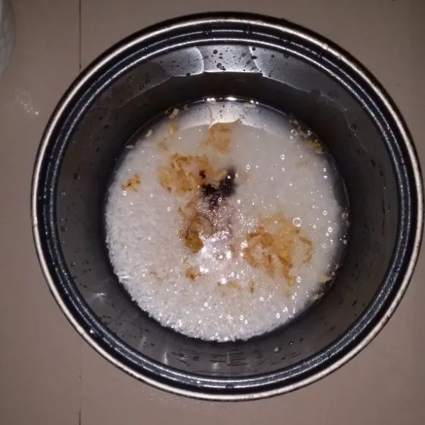 Siapkan teflon magic com. Masukan beras, air, garam, kaldu bubuk dan kecap manis. Kemudian tuang bawang putih goreng beserta minyaknya. Aduk hingga bumbu tercampur rata.