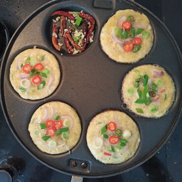 Panaskan pan. Tuang kocokan telur. Kemudian tutup rapat. Sangrai cincangan bawang putih , cabe kering dan daun bawang sebagai garnis. Cek bagian bawah telur dadar, apabila berwarna kecoklatan dan kering. Angkat dan tiriskan.