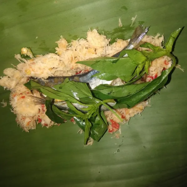 Siapkan daun pisang, lalu ambil kelapa parut berbumbu secukupnya, lalu letakkan ikan asin dan daun kemangi di atasnya. Gulung daun pisang, lalu sematkan kedua ujung dengan lidi.