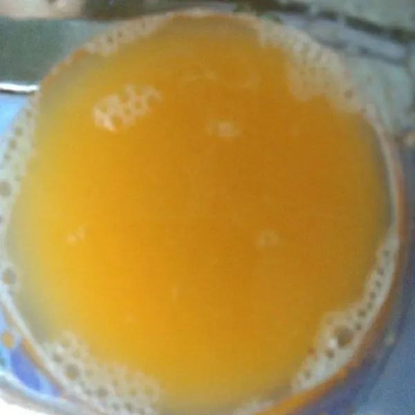 Saring air jeruk peras ke dalam gelas saji