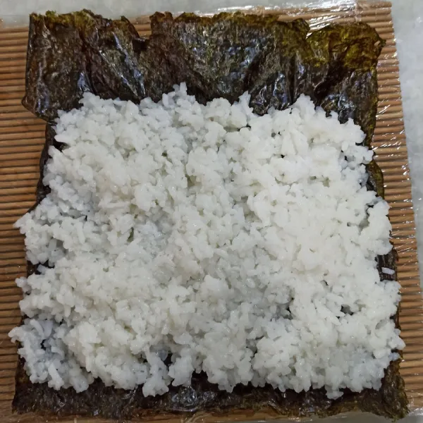 Letakan nasi di bagian nori yang halus (tampak tidak berkilau) dengan rata