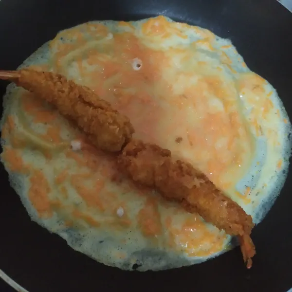 Panaskan teflon dengan api kecili, tuang adonan Tamagoyaki, ratakan, letakkan 2 ebi furai pada ujung, gulung, sisakan ujungnya.