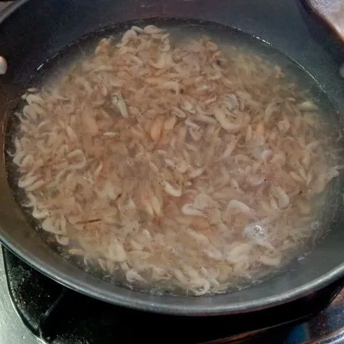 Rebus udang rebon dalam air mendidih, tambahkan bawang putih geprek, tunggu 5 menit sampai udang berubah warna.