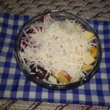 Taburi parutan keju pada permukaan salad buah.