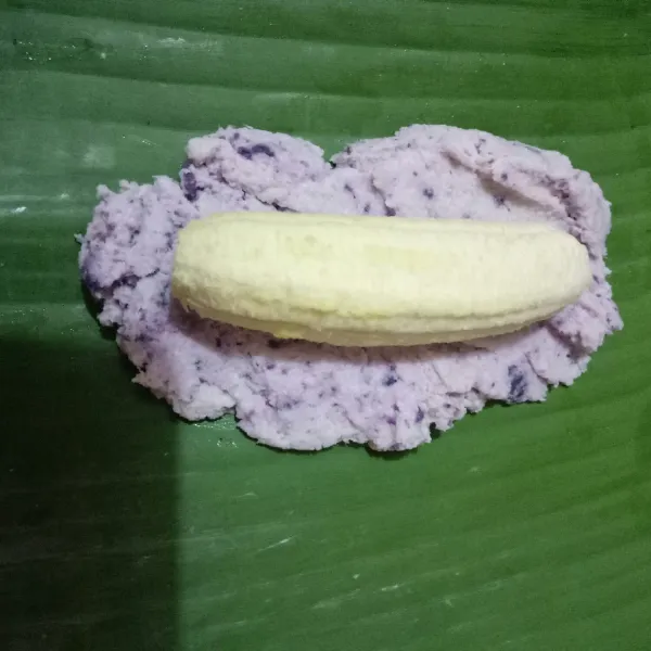 Siapkan daun pisang, ambil 1-2 sdm adonan ungu, lalu taruh pisang.