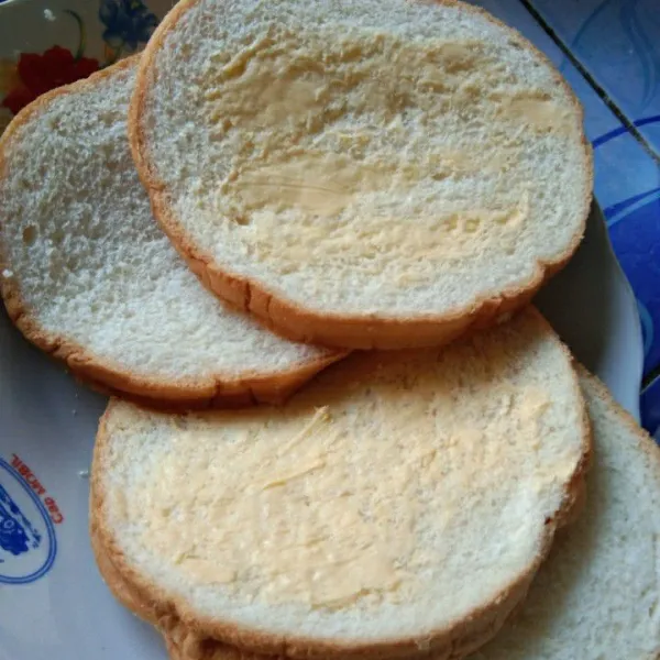 Olesi salah satu bagian sisi roti tawar dengan margarin.