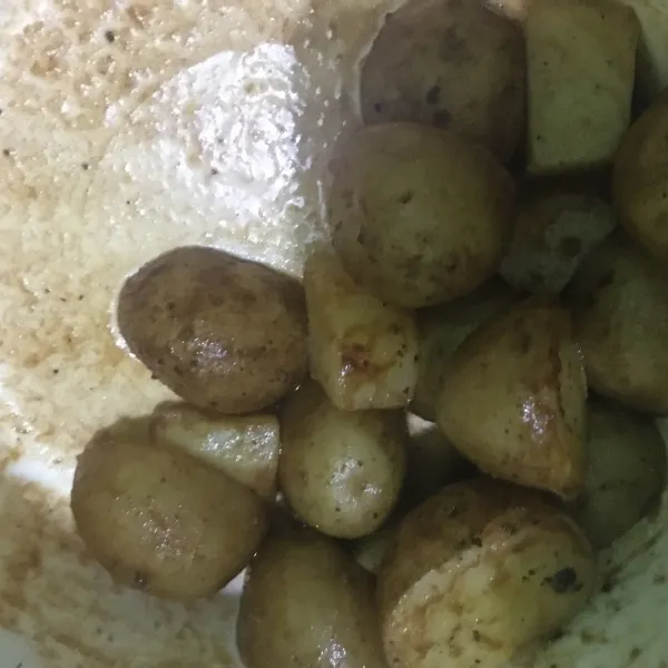 Masukkan kentang ke wadah bersih. Tambahkan lada hitam, cabai bubuk, garam, dan setengah bagian minyak bawang putih dan Rosemary. Aduk rata.