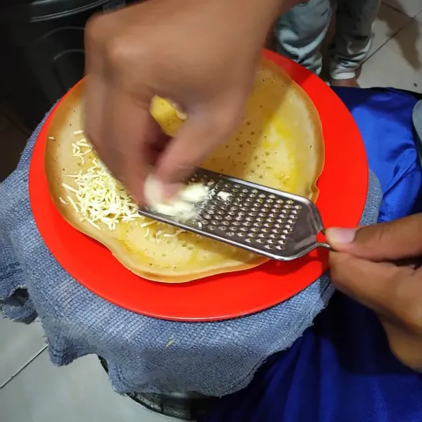 Lepaskan martabak dari loyang, olesi mentega lalu beri topping cokelat dan keju