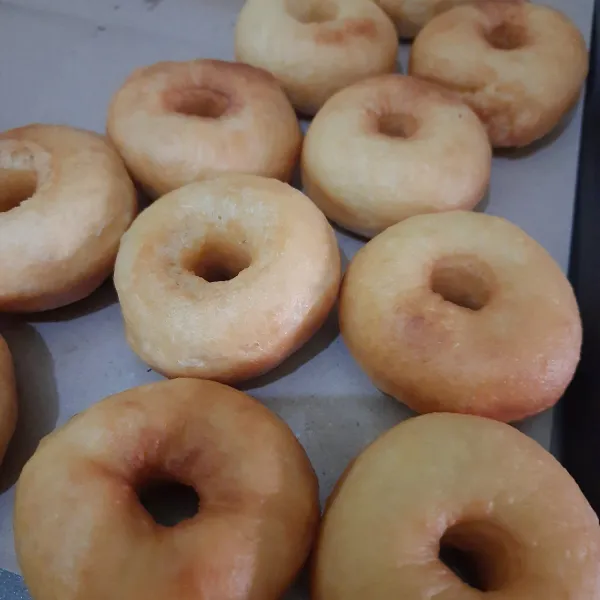 Donat sedang ditiriskan. Biarkan dingin lalu taburi dengan gula halus. Siap disantap.