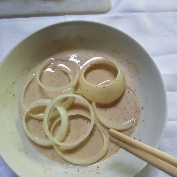 Celupkan bawang bombay ke adonan tepung bumbu menggunakan sumpit hingga semua bagian terkena.