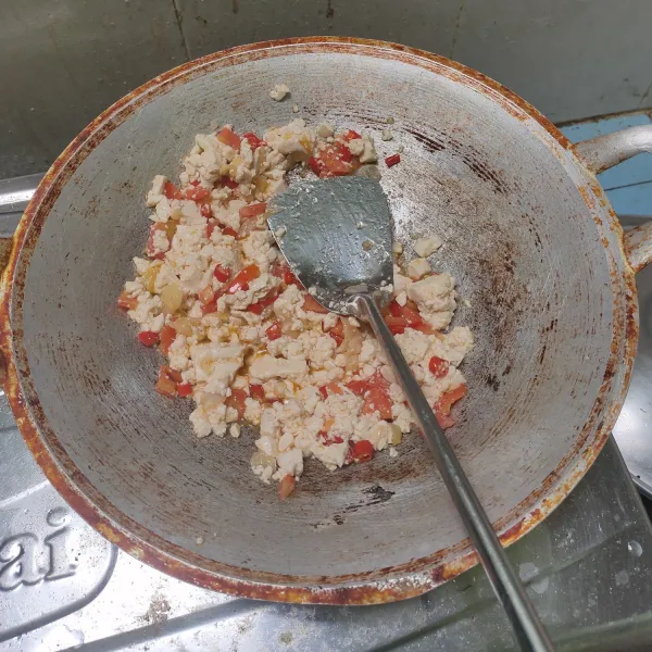 Tumis bawang merah, bawang putih dan cabe keriting hingga harum. Masukkan tahu dan tomat. Aduk-aduk hingga tahu merata dengan bumbu tumisan.