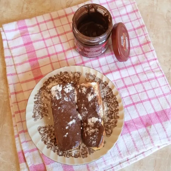 Sajikan eclair dengan olesan toping coklat dan taburan gula halus.
