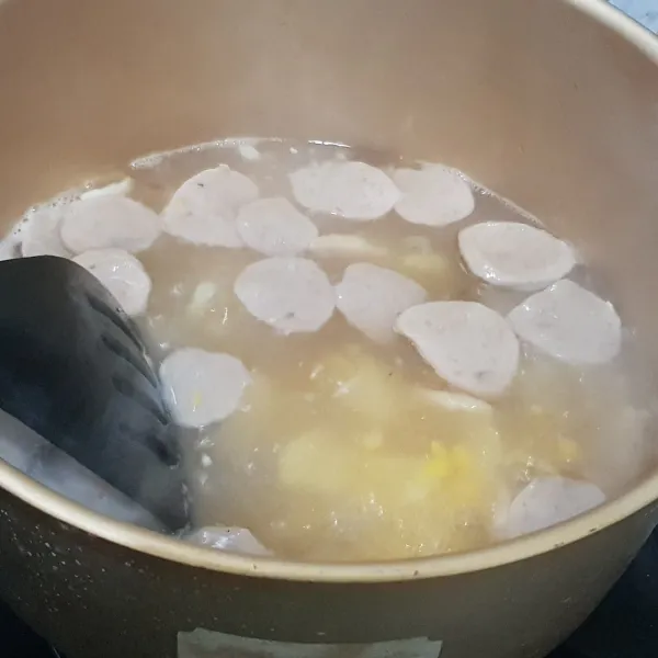Masukkan bawang putih yang sudah ditumis ke dalam air yang telah mendidih. Tambahkan bakso, wortel, dan jagung.