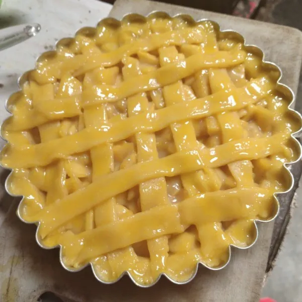 Bentuk 1/4 adonan kulit tipis memanjang, potong-potong. taruh diatas pie membentuk jaring. oles dengan kuning telur.