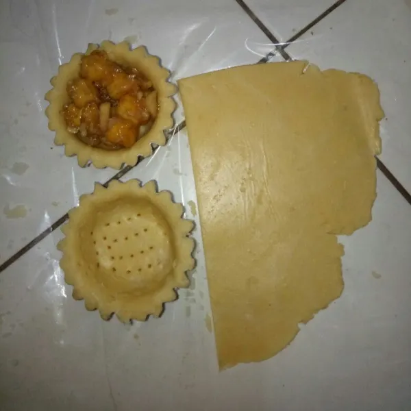 Setelah 30 menit, kulit pie siap digiling. Siapkan cetakan pie dan olesi margarin tipis - tipis. Pipihkan kulit pie sampai ketebalan 2 mm, cetak di cetakan pie lalu tusuk bagian bawah pakai garpu dan masukkan filling.