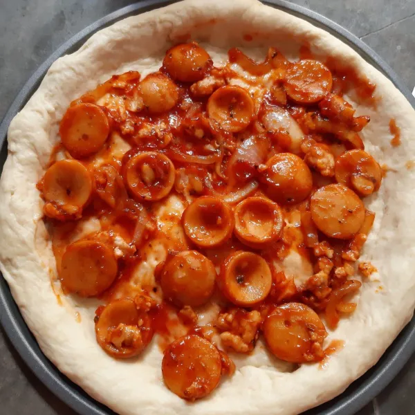 Cetak adonan ke dalam loyang pizza kemudian tusuk-tusuk dengan garpu, lalu beri topping sosis yang sudah ditumis