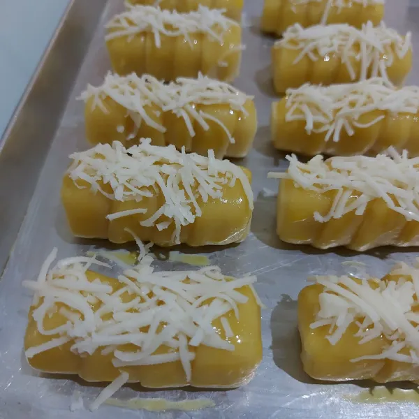 Tata cheese roll dalam loyang yg sudah dioles margarine. Oles dengan kuning telur dan taburi keju cheddar parut. Lakukan sampai selesai.