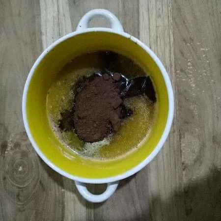 Masukkan cokelat cincang dan 10 gr cokelat bubuk ke mangkuk lalu siram dengan butter yang dilelehkan. Tunggu sekitar 2 menit agar coklat menjadi lunak.